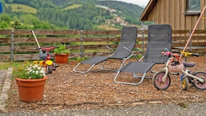 Une clôture en bois, deux fauteuils de jardin, un petit vélo et une plante en pot.