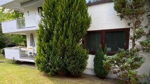 Une maison à deux étages avec un balcon, un grand arbre à feuilles persistantes et une pelouse bien entretenue.