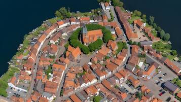 Une vue aérienne d’une ville avec une place centrale, des rues étroites et des bâtiments aux toits recouverts de tuiles rouges.