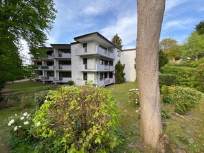 A multi-story residential building with balconies, surrounded by greenery and trees.