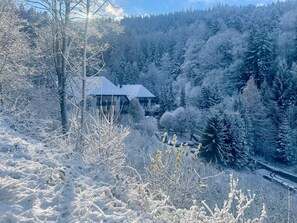 Schneebedeckte Landschaft mit einem Gebäude im modernen Stil, umgeben von dichtem Wald.