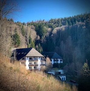 Ein zweistöckiges Gebäude mit geneigtem Dach, umgeben von bewaldeten Hügeln.