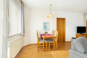 A room with a wooden dining table, chairs, a television, and a grey sofa.