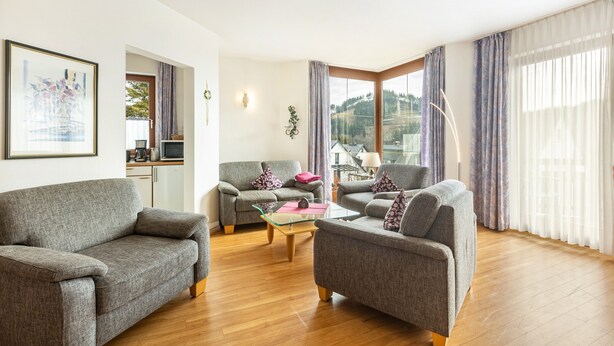 Een woonkamer met twee banken, een salontafel en uitzicht op een bergachtig landschap door grote ramen.