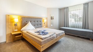 Een hotelkamer met een houten bed, nachtlampjes, een klein nachtkastje, een raam met gordijnen en uitzicht op buiten.