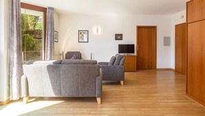 Amplia sala de estar con sofá, sillón y mueble para televisión, suelo de madera y puerta corredera.