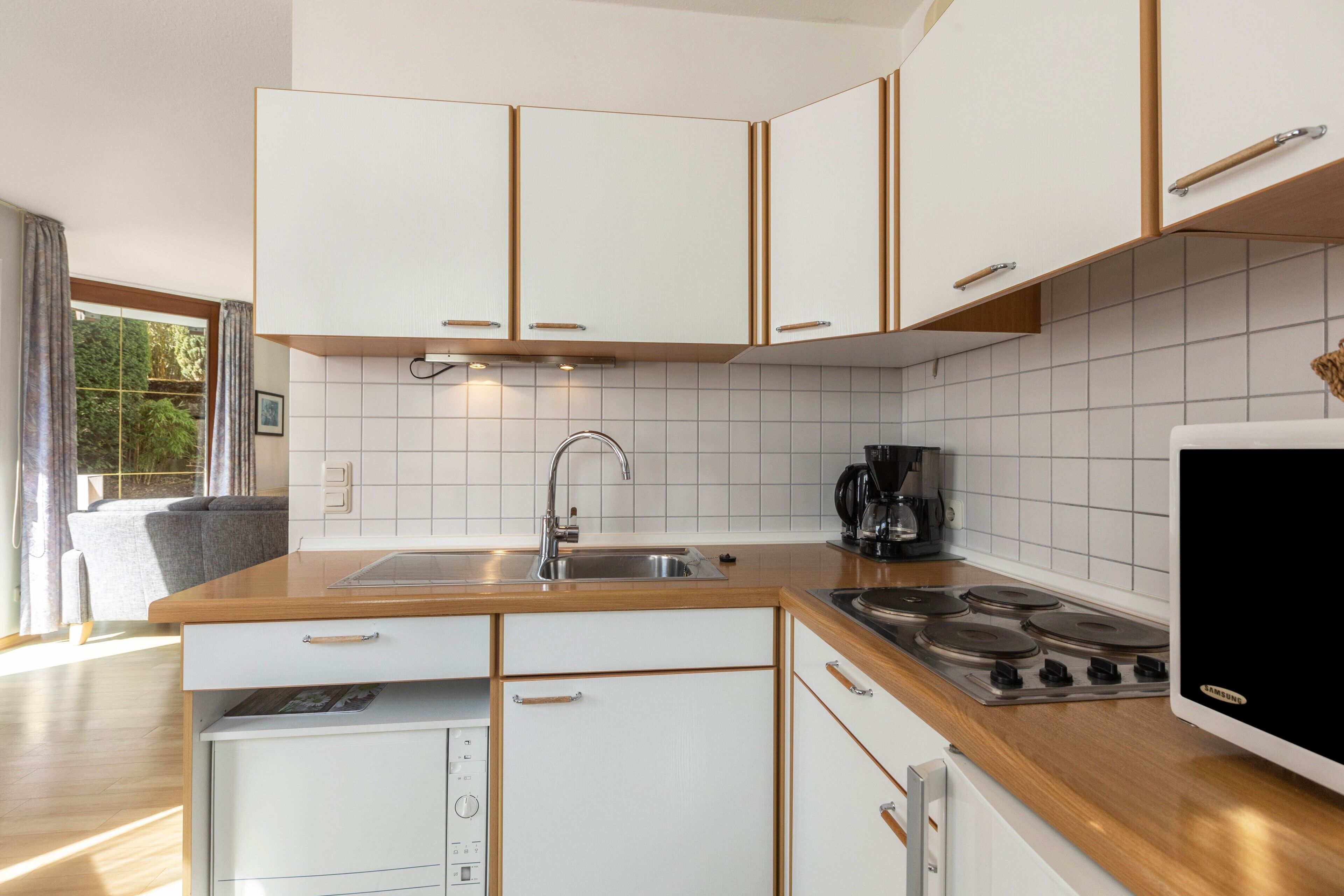 A modern kitchen with white cabinetry, a wooden countertop, a built-in stove, and a coffee maker.