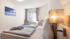 Una habitación de hotel con cama, ventana con cortinas, lámpara de pared y un cuadro en la pared.