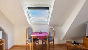 A room with a sloped ceiling, a skylight, a table with chairs, a small wooden table, and a telephone.