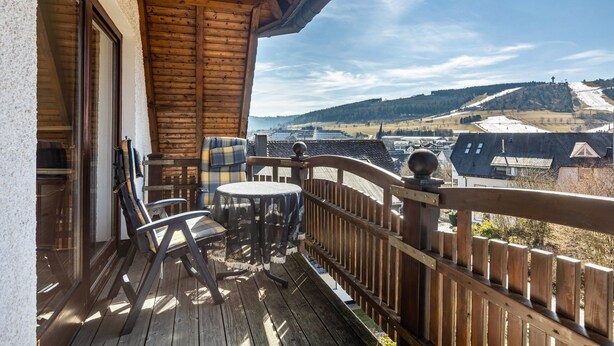A wooden deck with a table and chairs, overlooking a snowy landscape with buildings.