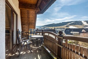 Een houten terras met een tafel en stoelen, met uitzicht op een besneeerd landschap met gebouwen.