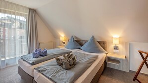 A hotel room with a bed, bedside lamps, a window with curtains, and a view of buildings outside.