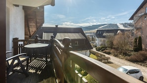 Ein Balkon mit Holztisch und Stühlen, Blick auf eine Wohngegend, und ein Auto auf der Straße geparkt.
