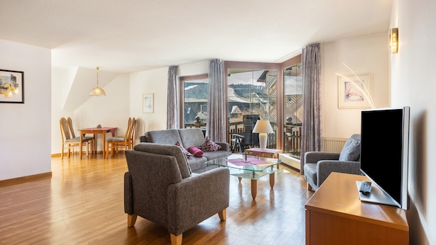 Ein modernes Wohnzimmer mit Sofa, Sessel, Glastisch und Flachbildfernseher.