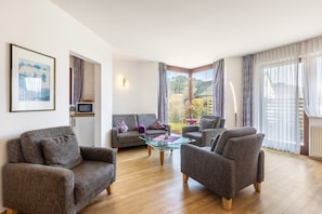 Una sala de estar con sofá, sillones, una mesa de centro de vidrio y vistas al exterior.