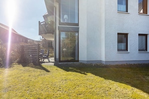 A modern two-story building with a balcony, large windows, and a grassy yard.