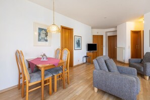 Una sala de estar con una mesa de comedor, dos sofás grises, sillas de madera, un televisor y un cuadro en la pared.