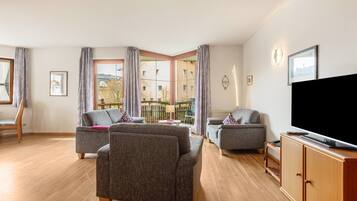 Ein Wohnzimmer mit zwei grauen Sofas, einem Holzkasten, einem Fernseher und einem Balkon mit Blick auf Gebäude.