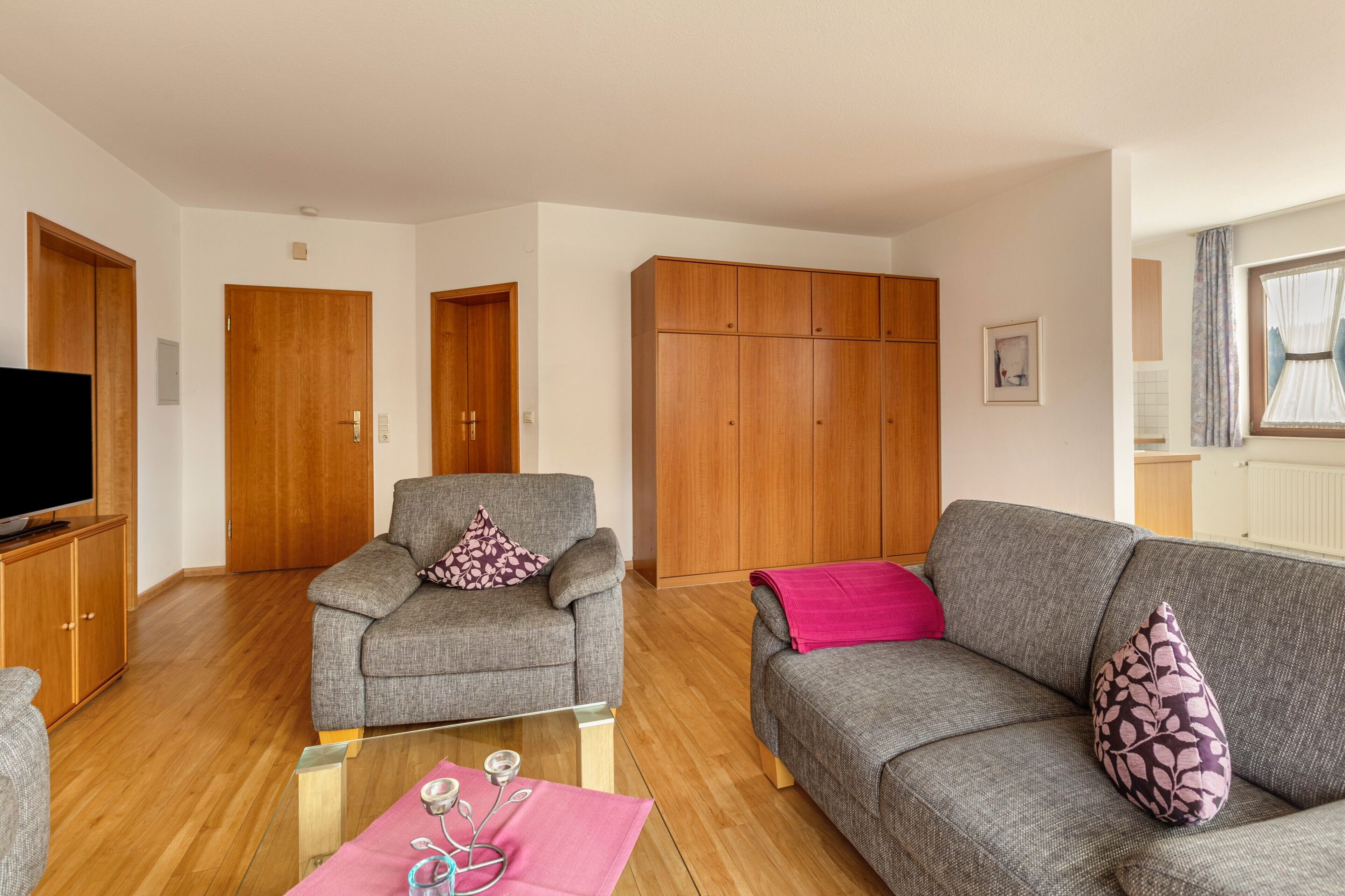 Ein Wohnzimmer mit zwei grauen Sofas, einem Holzschrank und einem Fernseher.