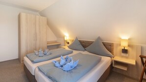 Et soveværelse med to senge, et træskab, sengeborde med lamper og et skråt loft.