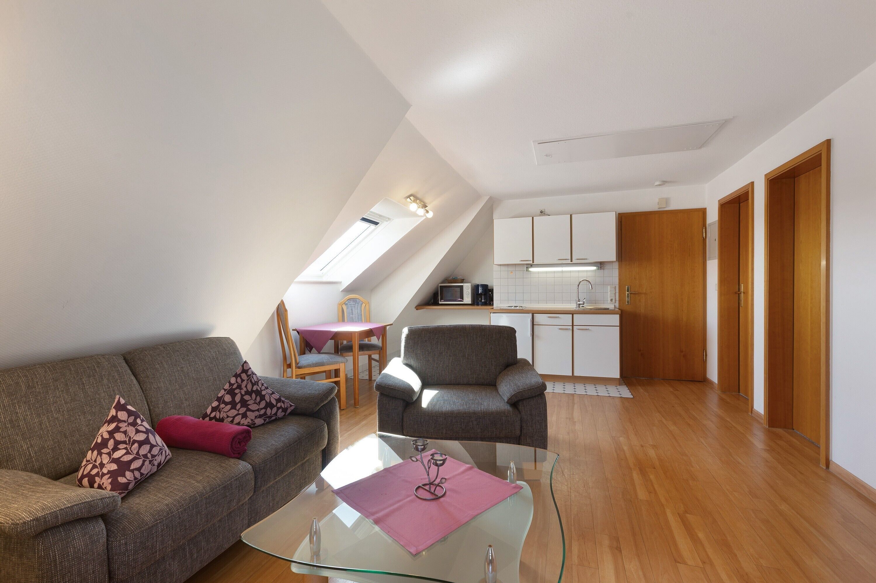 Una sala moderna con una mesa de centro de vidrio, un sofá con cojines estampados, un sillón gris y un comedor con mesa y sillas.