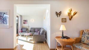 Un salon avec un canapé gris, une table en osier surmontée d’une lampe et des œuvres d’art décoratives accrochées au mur.