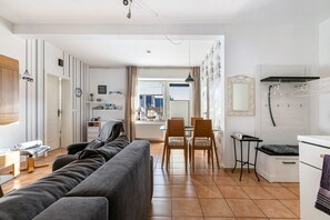 Un salon moderne comprenant un canapé, des fauteuils, une table à manger et un coin cuisine avec un réfrigérateur et un porte-vêtements suspendu.