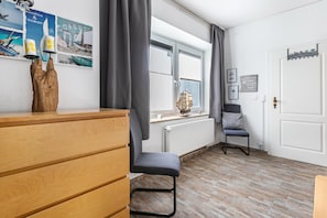 Une pièce comprenant une commode en bois, une chaise, une fenêtre avec des rideaux et des éléments de décoration murale, notamment un navire et un phare.