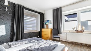 A bedroom with a bed, a desk, a chair, a dresser, and a window with blinds. - Holiday Apartment 'Friedrichskoog Spitze' with Private Terrace and Wi-Fi (Friedrichskoog)
