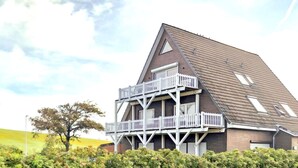 A two-story building with a balcony, surrounded by greenery. - Holiday Apartment 'Friedrichskoog Spitze' with Private Terrace and Wi-Fi (Friedrichskoog)