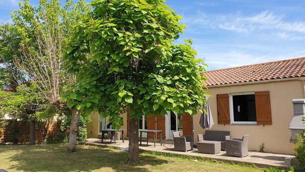 Ein Haus mit Terrasse, Gartenmöbeln und einem Baum.