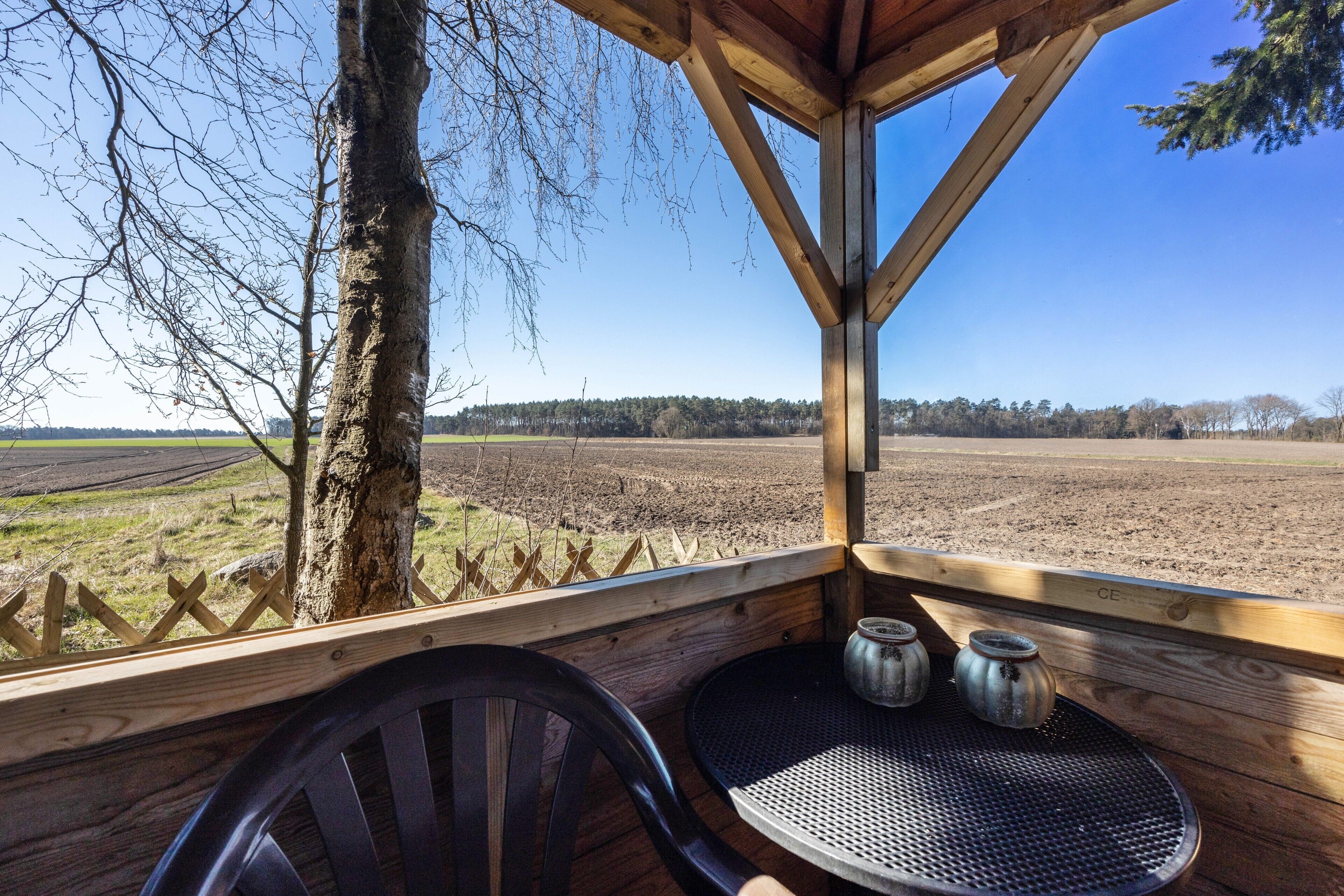 A wooden deck with a table and chairs, overlooking a field and trees.