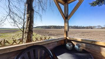 A wooden deck with a table and chairs, overlooking a field and trees.