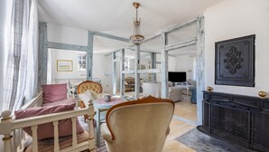 A room with a white bed, a chair, a fireplace, and a chandelier.
