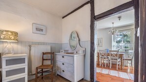 A room with a dresser, a chair, a mirror, a radiator, and a dining area with chairs and a table.