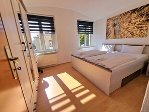 A bedroom with a bed, two windows, a radiator, and a painting on the wall. - Apartment 'Fewo Anne, Großzügige' with Private Terrace, Shared Garden and Wi-Fi (Chemnitz)