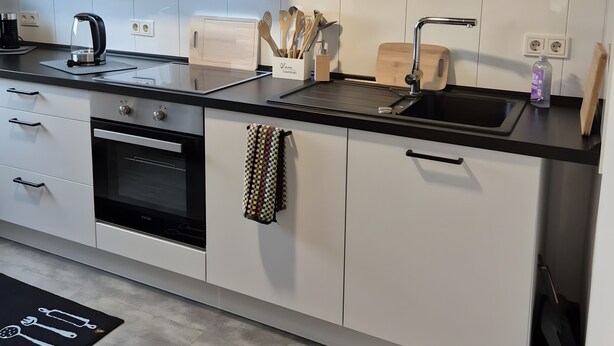 Una cocina moderna con armarios blancos, encimera negra, horno empotrado, hervidor y fregadero.