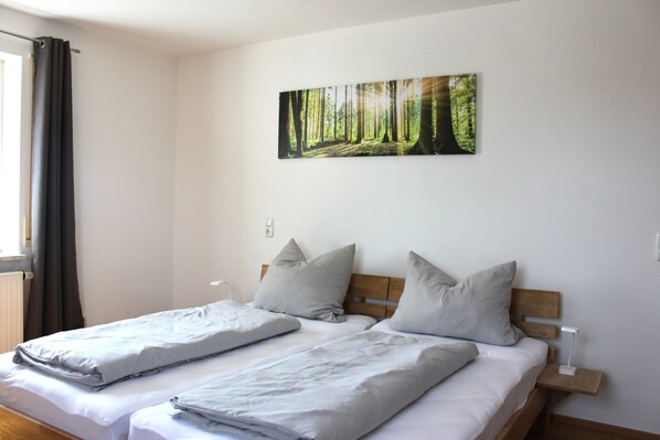 Un letto matrimoniale con testiera in legno, due cuscini, un comodino con una lampada e un quadro a tema bosco.