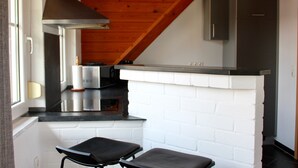 Una cocina con pared de ladrillo blanco, encimera negra, campana extractora de acero inoxidable y techo de madera.