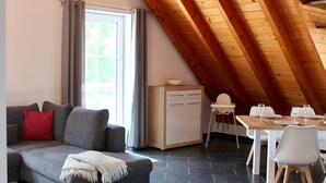 Un loft moderno con techo inclinado, un sofá con cojines, una mesa de comedor para dos personas y un mueble bajo.