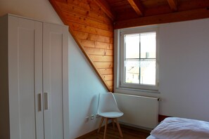 Une chambre avec un plafond en pente, une fenêtre, un radiateur et une chaise blanche.