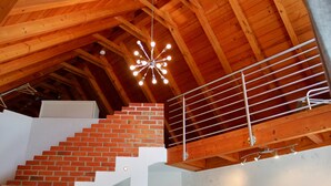 Una escalera de madera con pared de ladrillo, barandilla metálica y una lámpara colgante.