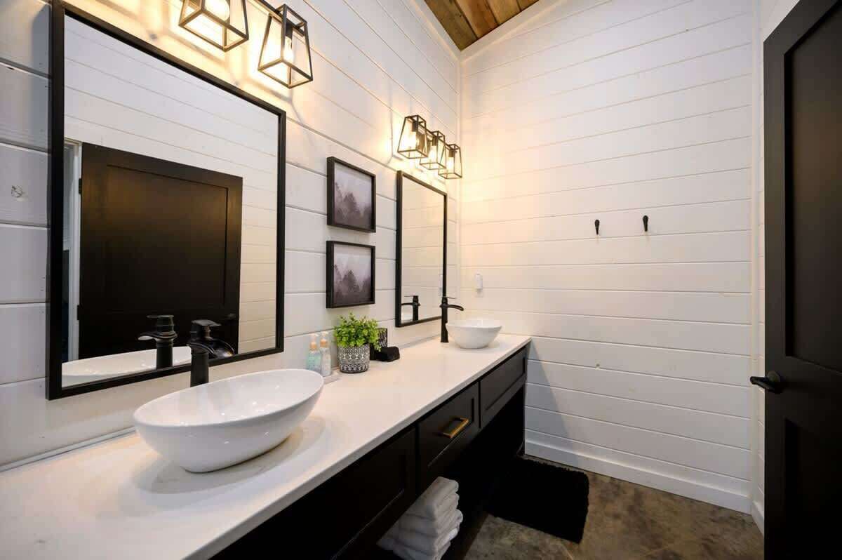 A modern bathroom with a white vanity, black fixtures, and framed pictures on the wall.