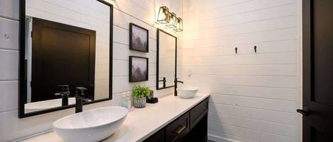 A modern bathroom with a white vanity, black fixtures, and framed pictures on the wall.