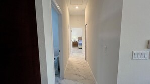 A hallway with a marble floor leading to a bedroom with a bed and a nightstand.