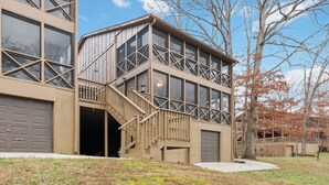 A two-story building with a large garage door, a staircase leading to a balcony, and a tree with autumn leaves.