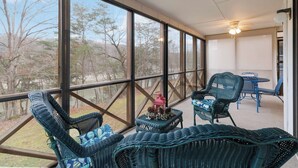 A covered patio with wicker furniture, a table, and chairs, overlooking a wooded area.