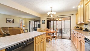 A kitchen with wooden cabinets, a dishwasher, a dining table with chairs, and a chandelier.