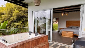 A modern outdoor bathroom with a wooden bench, a hot tub, and a glass door leading to a bedroom with a bed and a wooden headboard. - GLAMPING WITH POOL AND JACUZZI AT GUATAPE  (Antioquia)