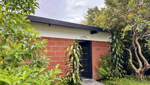 A small building with a brick facade and a black door, surrounded by lush greenery and trees. - GLAMPING WITH POOL AND JACUZZI AT GUATAPE  (Antioquia)